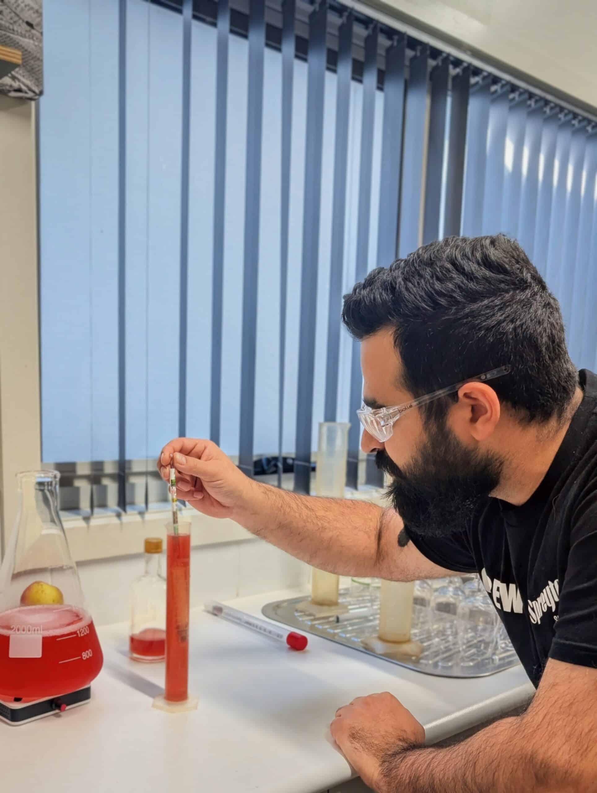 A person wearing safety spectacles measures red liquid in a graduated cylinder in a laboratory.