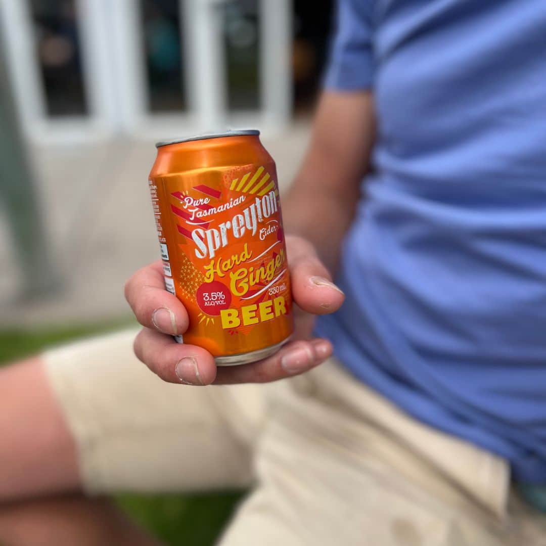 Person in a blue shirt and beige shorts holding a can labelled "Spreyton Hard Ginger Beer.