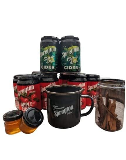 Cider cans labelled "Spreyton," a black mug, two small jars of honey, and a glass jar of cinnamon sticks arranged together.